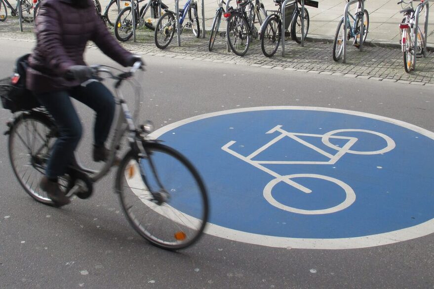 Fahrrad fährt über eine Straße mit runder Grafik mit weißem Fahrrad auf blauem Hintergrund