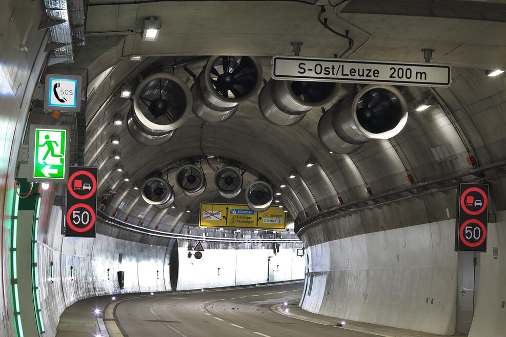 Blick aus dem Rosensteintunnel in Richtung eines Tunnelportals. Es sind die Lüftungsventilatoren, Verkehrszeichen  sowie die Straßenmarkierung im Tunnel zu sehen.