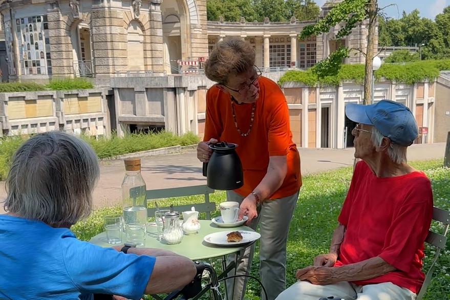 Three women sit at a table with coffee and cake at the Prague Cemetery