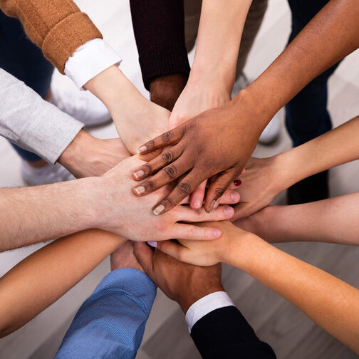 Mehrere Menschen stehen in einem Kreis und halten ihre Hände in der Mitte zusammen.