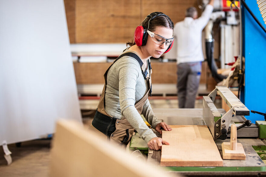 Eine Tischlerin legt ein Holzbrett auf eine Werkbank.