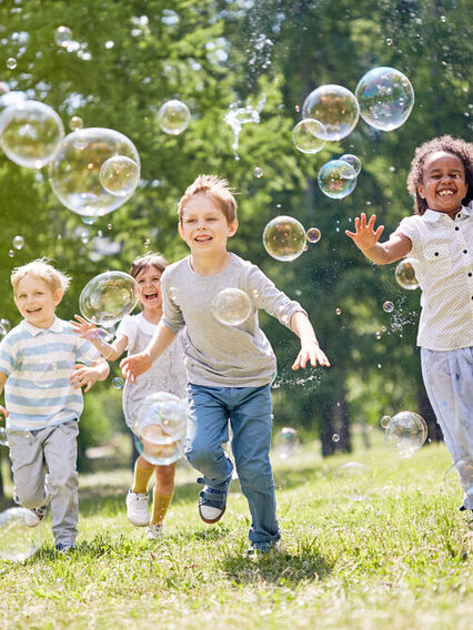 Kinder im Park rennen den Seifenblasen hinterher.