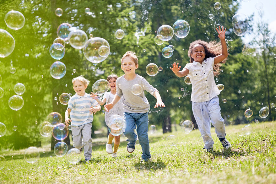 Kinder im Park rennen den Seifenblasen hinterher.