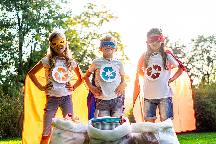 Gruppe von Kindern sammelt Müll in der Natur: Vor ihnen liegen Säcke mit Plastikflaschen, Papier und anderem Müll.