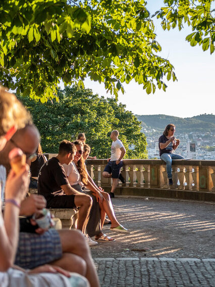 Menschen sitzen am Eugensplatz mit Blick von oben auf die Innenstadt.