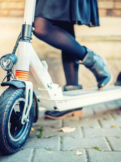 Nahaufnahme vom E-Scooter: Ein Frau steht mit schwarzen Schuhen auf einem E-Scooter.