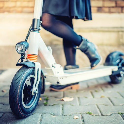 Nahaufnahme vom E-Scooter: Ein Frau steht mit schwarzen Schuhen auf einem E-Scooter.