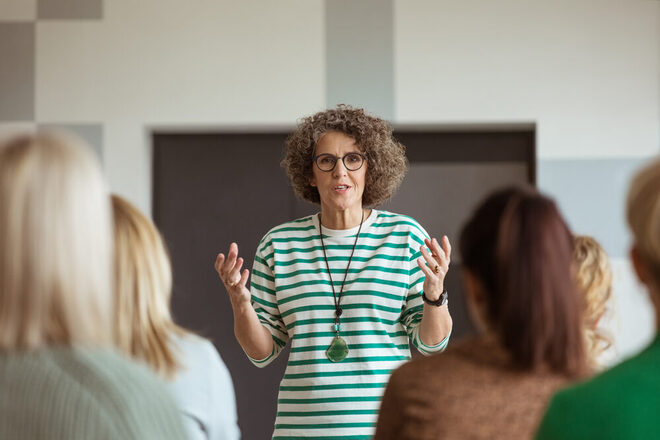 Workshop-Situation: Eine Frau in einem grün-weiß gestreiften Pullover spricht vor Zuhörern.