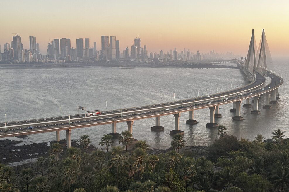 Skyline von Mumbai. Im Vordergrund eine große Hängebrücke, die eine Bucht überquert.