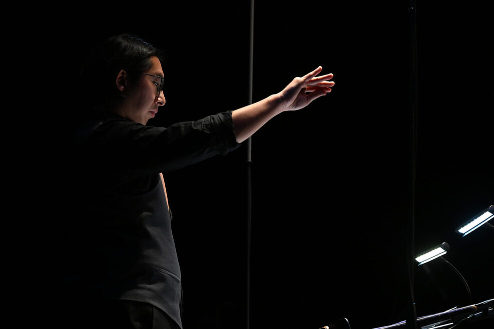 Ein schwarz gekleideter Dirigent bei der Arbeit auf der Bühne.