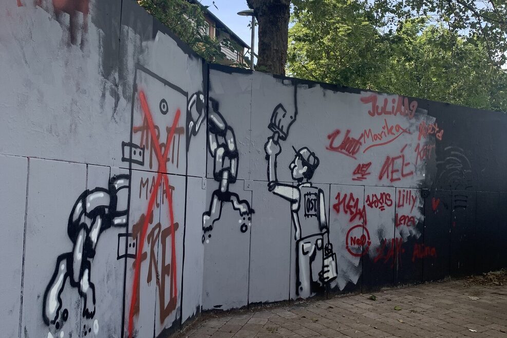 In Grautönen gehaltenes Graffiti an einer Mauer.