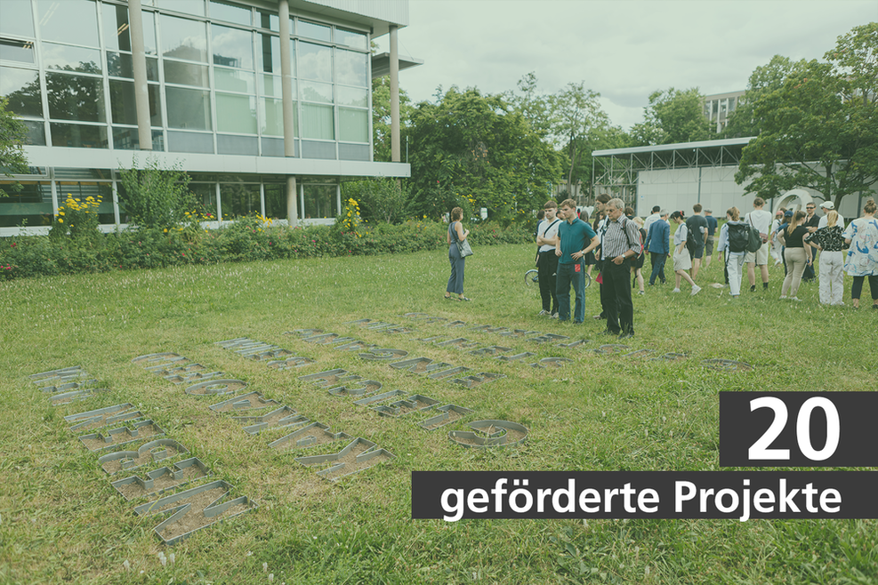 Mehrere Personen betrachten einen Schriftzug aus Metal in einer Wiese. Schriftzug "20 geförderte Projekte".