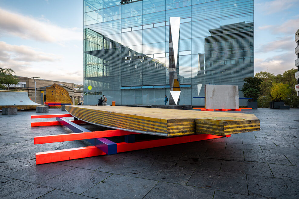 Eine Installation auf dem Kleinen Schlossplatz in Stuttgart, mehrere bunte Latten und Bretter wurden übereinandergelegt. Im Hintergrund ist das Stuttgarter Kunstmuseum zu sehen.