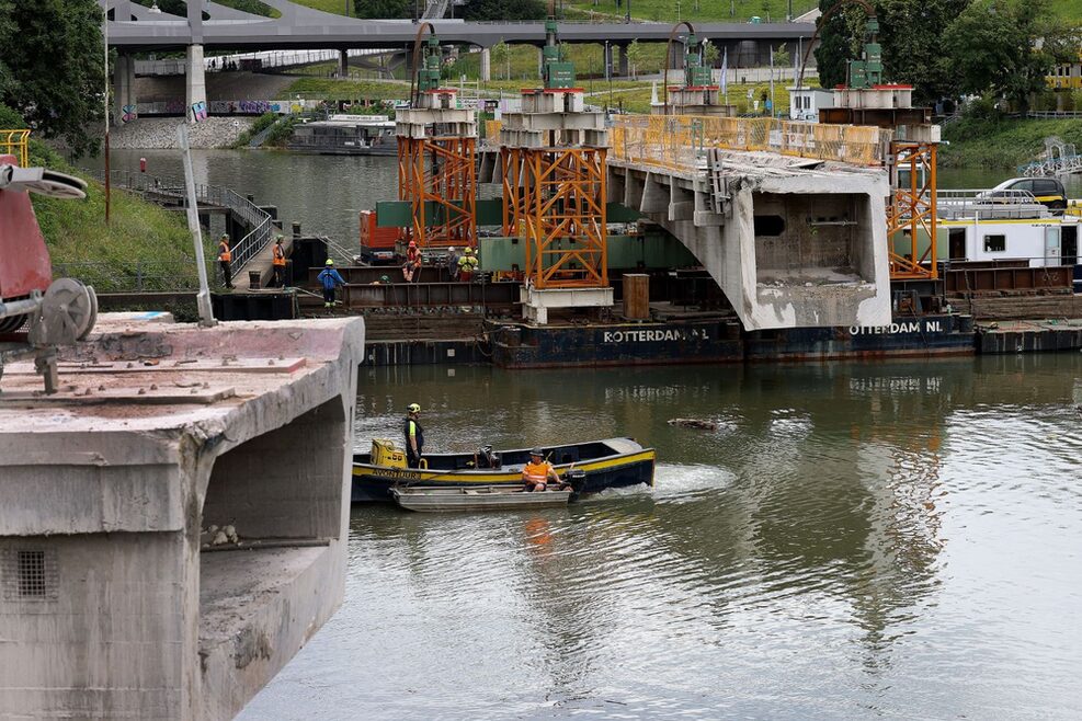 Einige Arbeiter befinden sich auf der schwimmenden Arbeitsplattform. Über ihnen ragt der verbliebene Brückenträger über den Neckar.