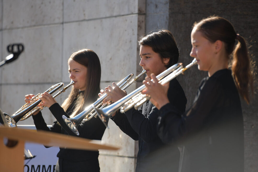 Drei Musikschüler spielen vor dem Rathaus Trompete.