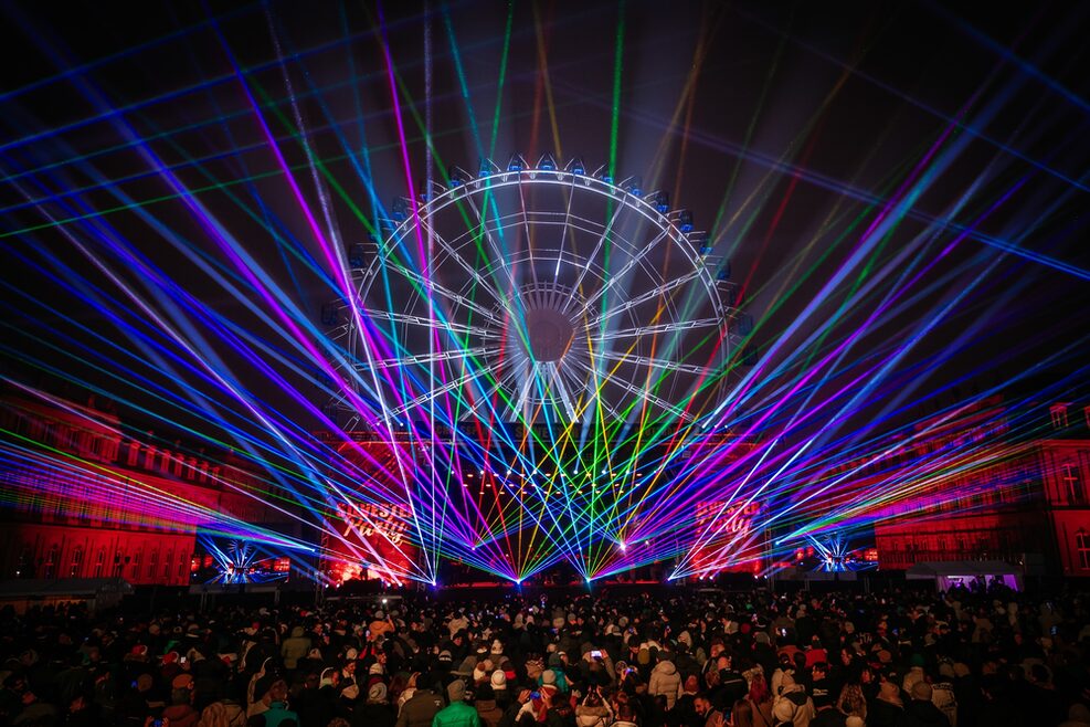 Blick auf den Schlossplatz mit feierndem Publikum, beleuchtetem Riesenrad und Lasershow.