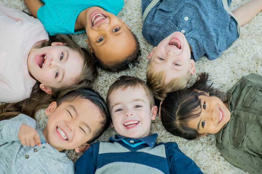 Sechs Kinder liegen im Kreis auf dem Rücken und lachen.