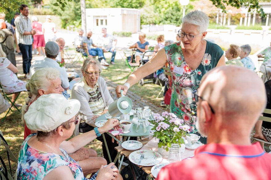 Pop-Up Cafe auf dem Pragfriedhof, Stuttgart. Menschen trinken unter freiem Himmel Kaffee und tauschen sich aus.