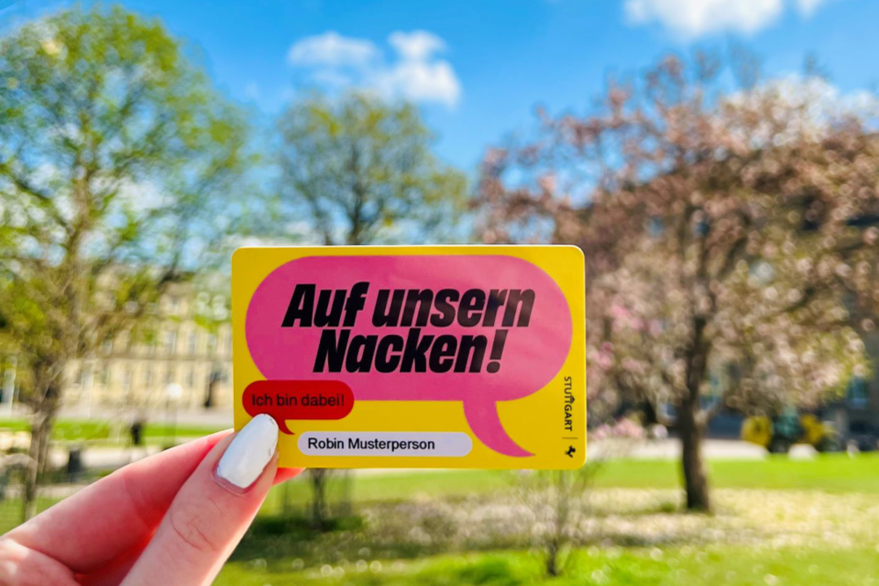 Das Bild zeigt eine Nahaufnahme des Kulturpasses. Der Pass ist so groß wie eine Bankkarte und aus gelbem Plastik. Darauf ist zu lesen. "Auf unsern Nacken! Ich bin dabei!" und der Name "Robin Musterperson". Am Rand der Karte ist noch das Stuttgarter Rössle und der Schriftzug "Stuttgart" zu sehen.