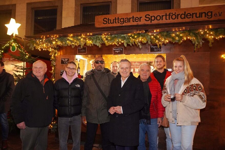 Im Hintergrund ist der Stand der Stuttgarter Sportförderung e.V. auf dem Weihnachtsmarkt zu sehen. Im Vordergrund stehen von Links Präsident der Sportförderung Harald Müller, Schwimmerin Linda Roth, Blindenfußballer Mulgheta Russom, OB Dr. Frank Nopper, Rene Tschur, Sportkreispräsident Fred-Jürgen Stradinger, Patrick Thumm und Volleyballerin Jelena Wlk vor dem Stand der Sportförderung.