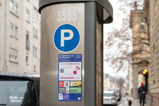 Ein Parkautomat mit einem Aufkleber, auf dem verschiedene QR-Codes abgebildet sind.