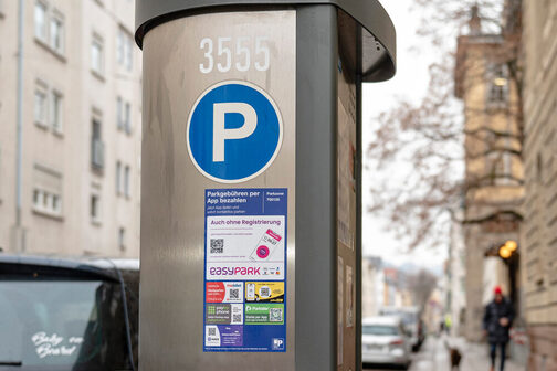 Ein Parkautomat mit einem Aufkleber, auf dem verschiedene QR-Codes abgebildet sind.