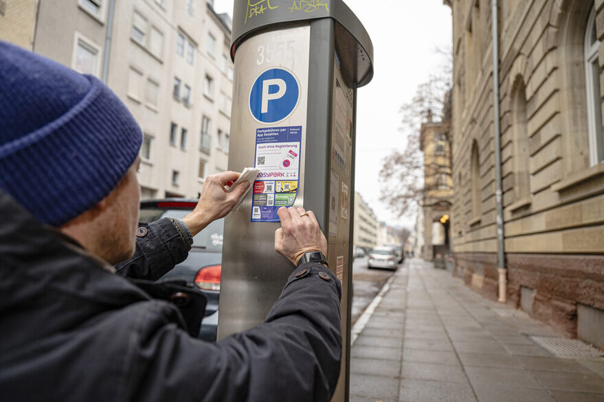 Ein Mann bringt einen Aufkleber an einem Parscheinautomaten an.