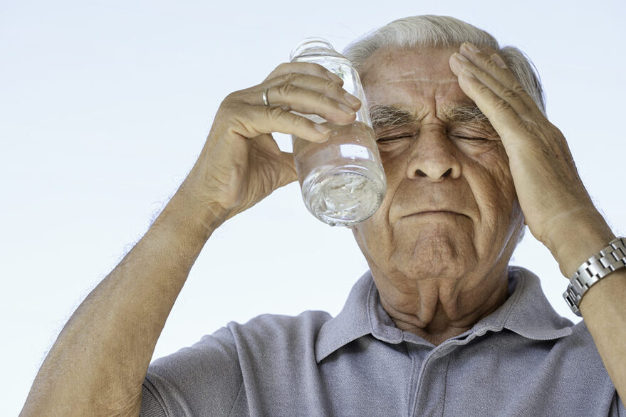 Ein älterer Herr kühlt seinen Kopf mit einer Wasserflasche, die er gegen die Schläfe hält.