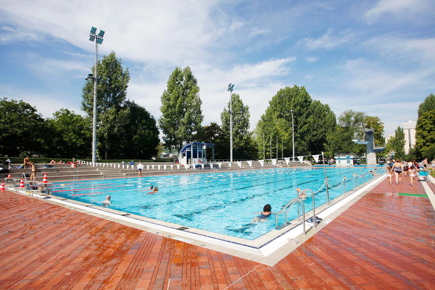 Das Sportbecken im Inselbad bei schönem Wetter. Nur wenige Badegäste schwimmen im Becken, einige sind außerhalb des Beckens unterwegs.