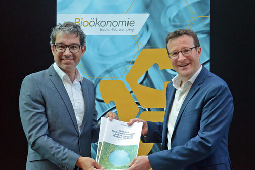 Staatssekretär Dr. Andre Baumann (links) und Martin Körner, Leiter des Grundsatzreferates für Klimaschutz, Mobilität und Wohnen der Stadt Stuttgart mit einem Exemplar der Bioökonomiestrategie der Stadt Stuttgart.