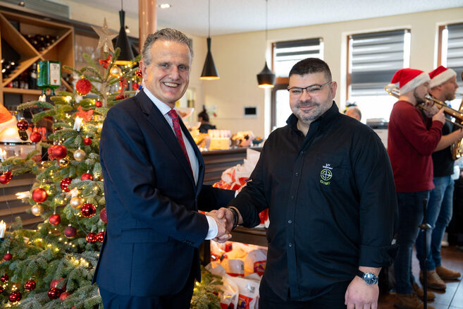 Weihnachten 2023: OB Nopper zu Besuch bei Dimitrios Evangelopoulus von „Dimi hilft“ in Weilimdorf, sie begrüßen sich mit Handschlag, im Hintergrund steht ein geschmückter Weihnachtsbaum