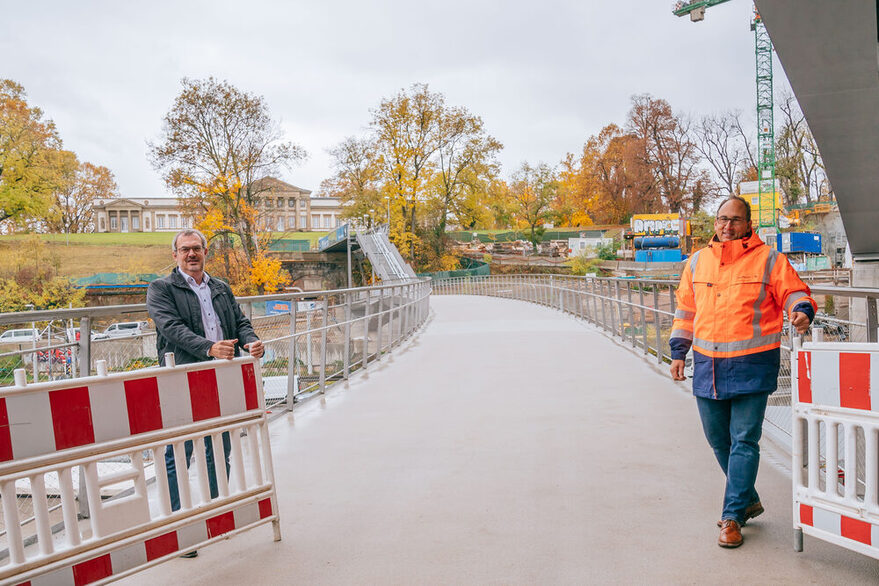 Blick auf den neuen STeg von der Bastion unter der neuen S21-Brücke aus in Richtung Rosensteinpark. Im Vordergrund steht der Leiter des Tiefbauamts, Jürgen Mutz, rechts und Georg Wilhelm, zuständig für Stadtbahn, Brücken und Tunnelbau, Koordination Bauausführung Gesamtprojekt B10 Rosensteintunnel, links. Es ist der geschwungene Steg zu sehen mit der provisorischen Treppenanbindung und dem Schloss Rosenstein im Hintergrund.