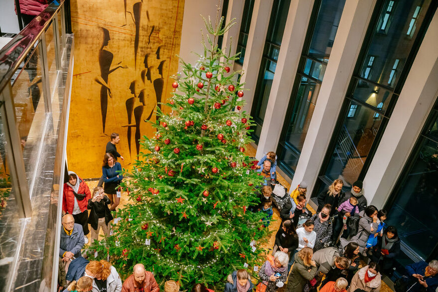 Der Weihnachtsbaum der Kinderwünsche aus dem Jahr 2022 ist zu sehen. Neben dem Weihnachtsbaum stehen interessierte Personen