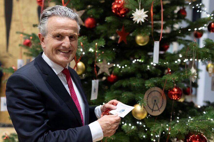 Oberbürgermeister Frank Nopper pflückt eine Wunschkarte vom Weihnachtsbaum der Kinderwünsche.