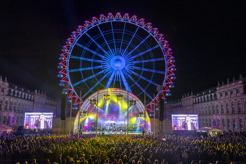 Publikum und Showbühne vor dem leuchtenden Riesenrad am Neuen Schloss