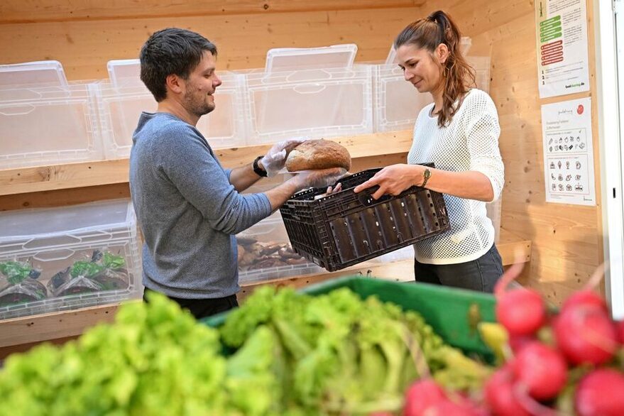 Eine Frau und ein Mann in einem Fairteiler, wo sie Lebensmittel in eine Kiste packen.