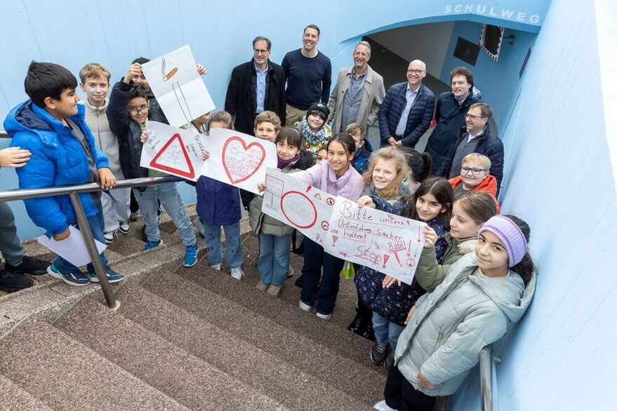 Kinder und Erwachsene stehen mit gebastelten Verkehrsschildern der Kinder vor der Unterführung.