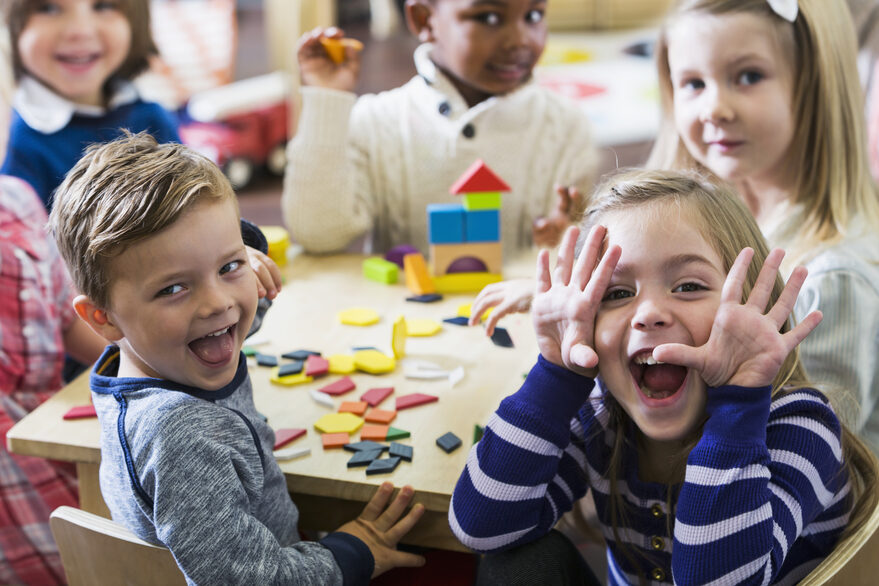 Kinder sitzen um einen Tisch und schneiden Grimassen