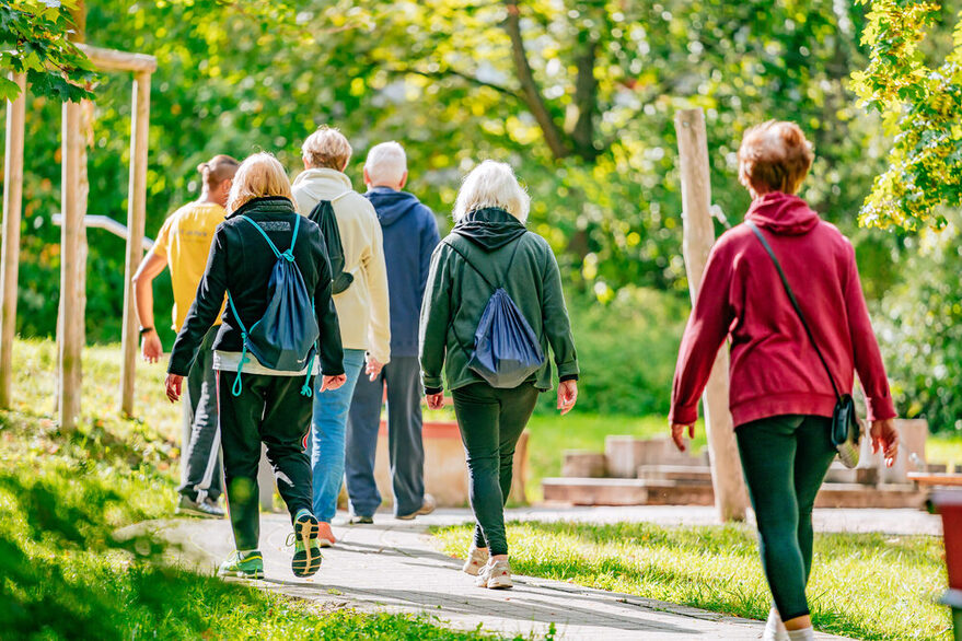 Eine Gruppe älterer Menschen (6 Personen) beim Stadtteilspaziergang im Grünen.