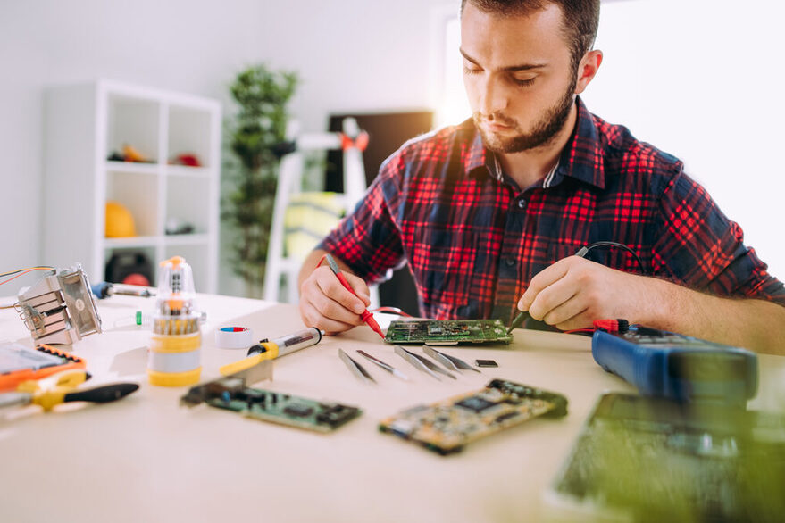 Ein junger Mann repariert eine elektronischen Platine.