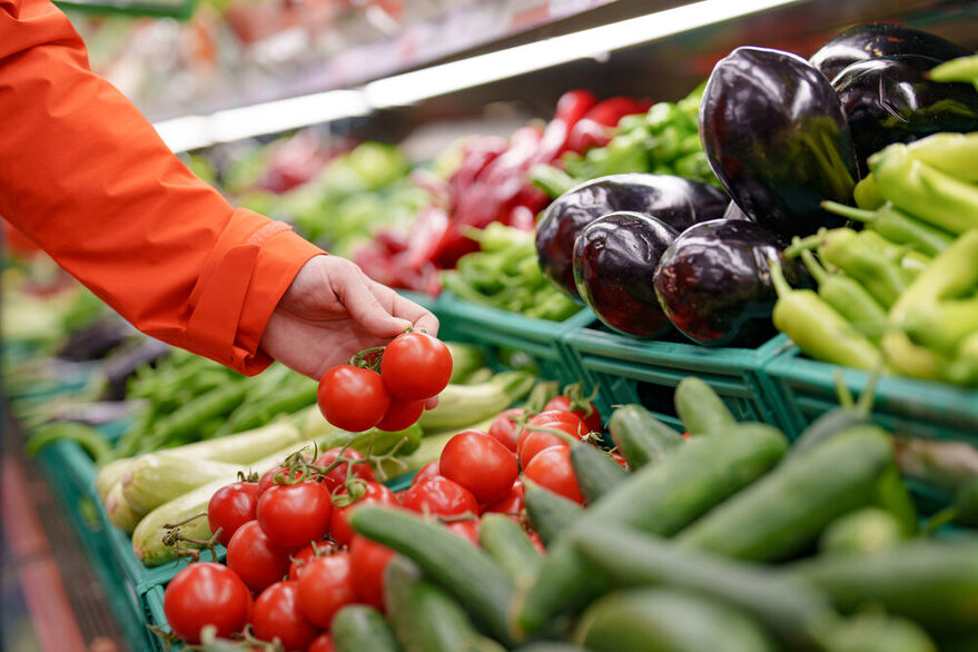 Hand greift nach Tomaten in der Gemüse Abteilung eines Supermarktes