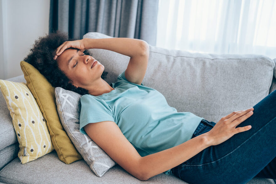 Eine Frau liegt krank auf der Couch.