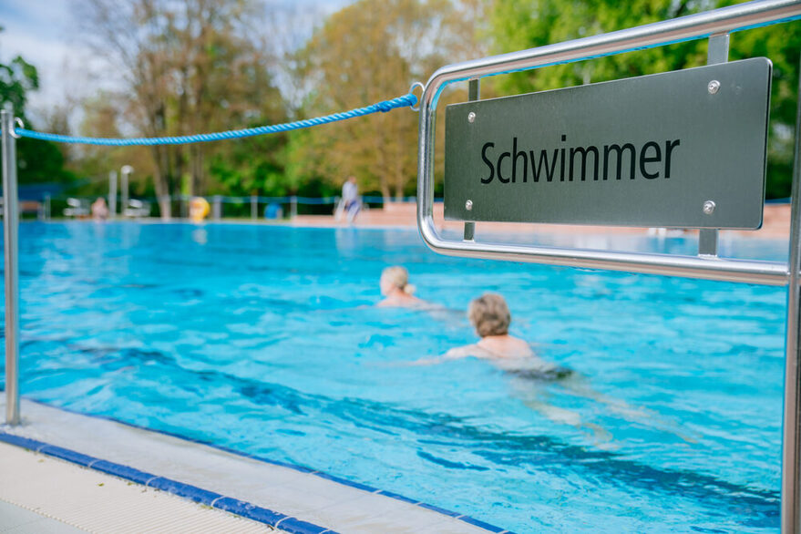 Im Hintergrund: Zwei Personen schwimmen im Pool des Freibads Möhringen. Im Vordergrund: Ausschilderung des Schwimmer-Bereichs.