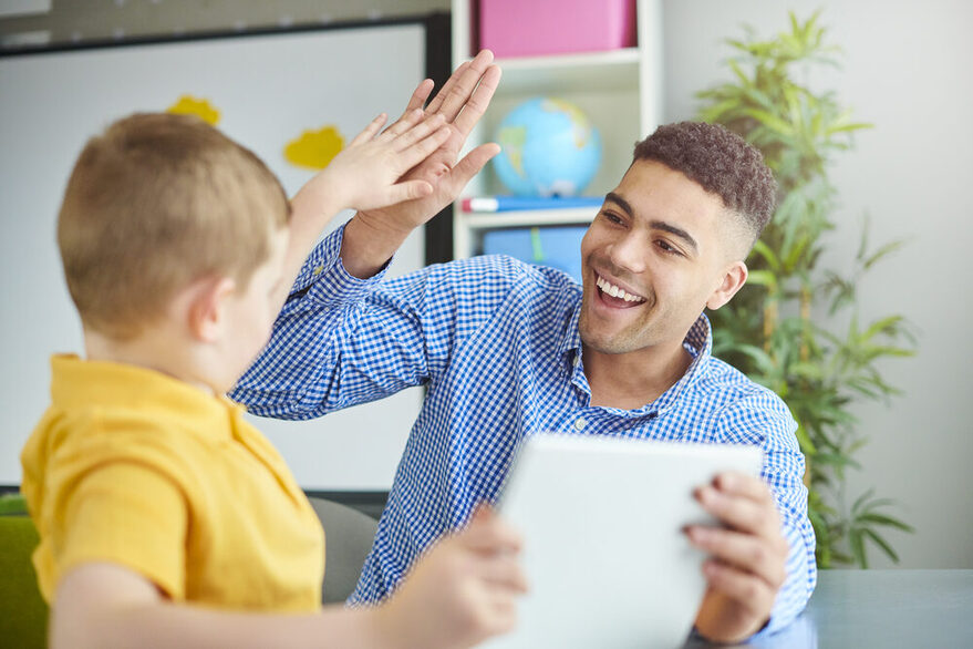 Ein Junge und ein junger Mann geben sich ein High-Five und halten gemeinsam ein Tablet in den Händen.