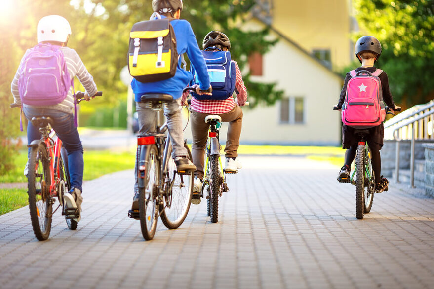 Children with rucksacks riding on bikes in the park near school