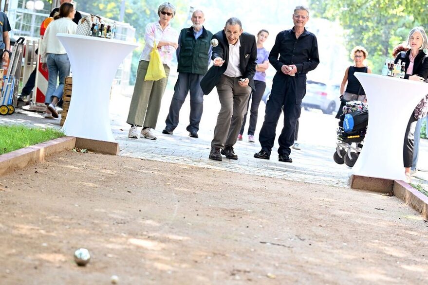 Auf dem Foto ist der Boule-Bereich des Aktivbands der Elisabethenanlage zu sehen. Der Bezirksvorsteher Bernhard Mellert spielt Boule. Im Hintergrund ist die Eröffnungsveranstaltung und Gäste zu sehen.