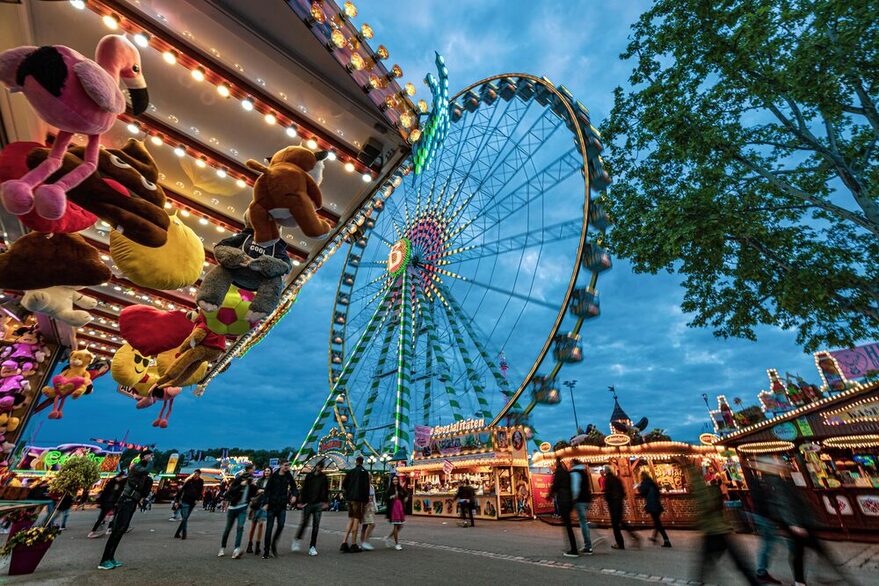 Bild vom Cannstatter Wasen Gelände in der Dämmerung mit Riesenrad und beleuchteten Buden.