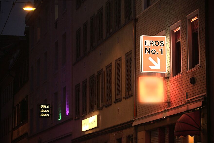 Hausfassade im Dunkeln, neonbeleuchtetes Schild mit dem Titel "Eros No. 1"