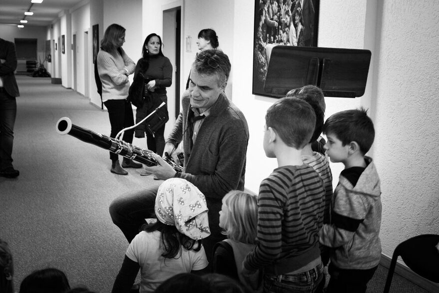 Ein schwarz-weiß Foto, das zeigt, wie ein Person mehreren Kindern ein Instrument erklärt.