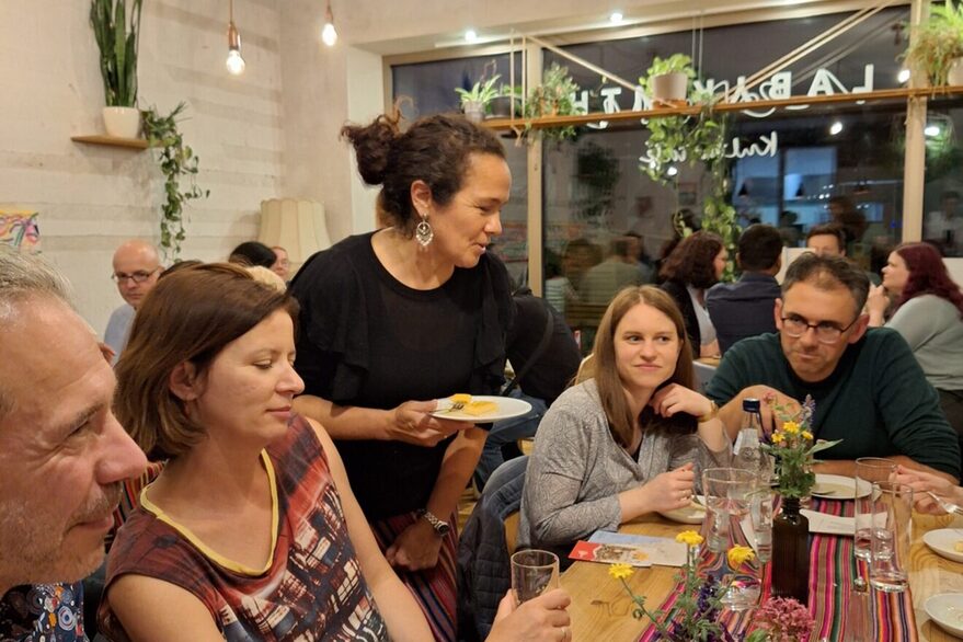 Personen sitzen gemeinsam bei Tisch, unterhalten sich und essen zu Abend.